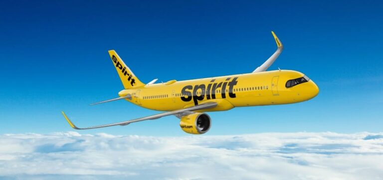 Yellow Spirit Airlines jet flying above clouds in a blue sky.