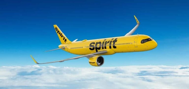 Bright yellow Spirit Airlines jet flying above clouds in a blue sky