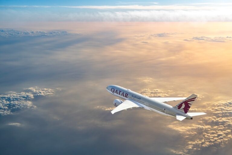 Qatar Airways aircraft flying above clouds at sunset.