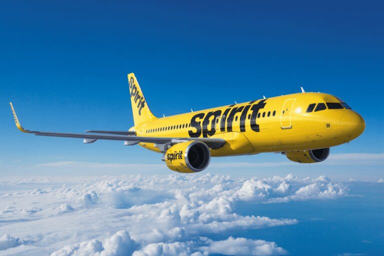 Yellow Spirit Airlines jet flying above clouds against a blue sky.