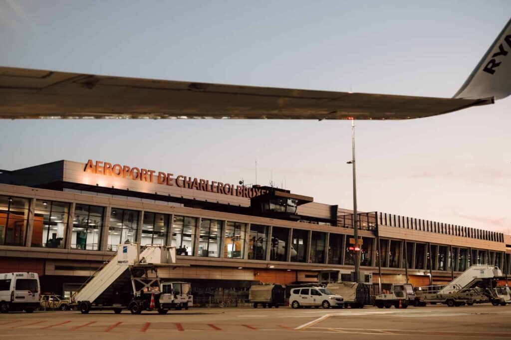 Airplane wing over Charleroi Brussels Airport terminal with glass walls and boarding bridge.