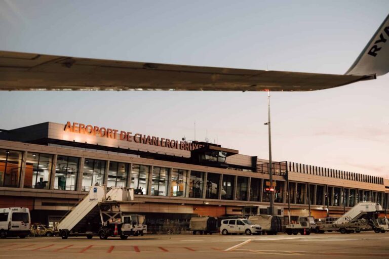 Airplane wing over Charleroi Brussels Airport terminal with glass walls and boarding bridge.