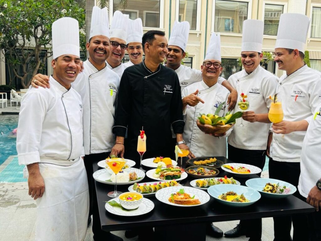 Group of chefs in white uniforms and tall hats posing by a banquet table with various dishes by a poolside.