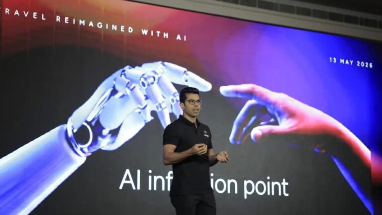 Speaker on a stage with a large screen showing robotic and human hands reaching toward each other and the text 'AI information point'.