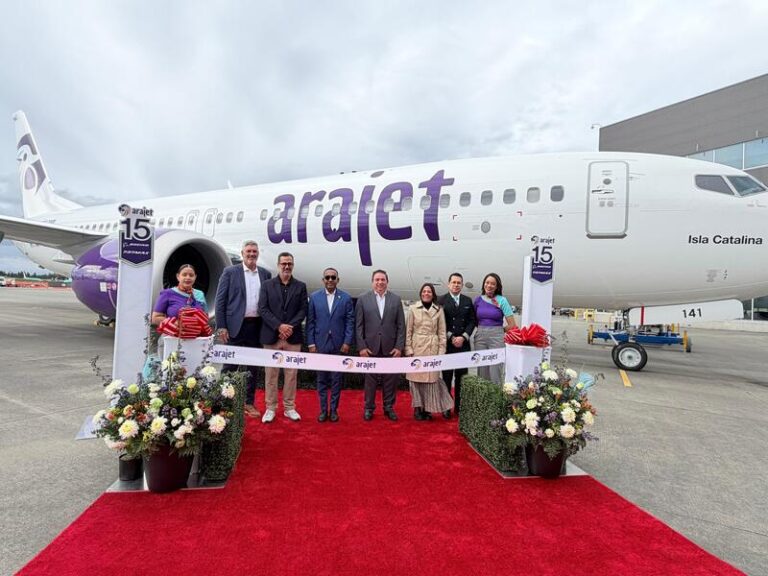 Group of people in formal attire pose on a red carpet in front of a branded Arajet airplane during a ribbon-cutting ceremony.