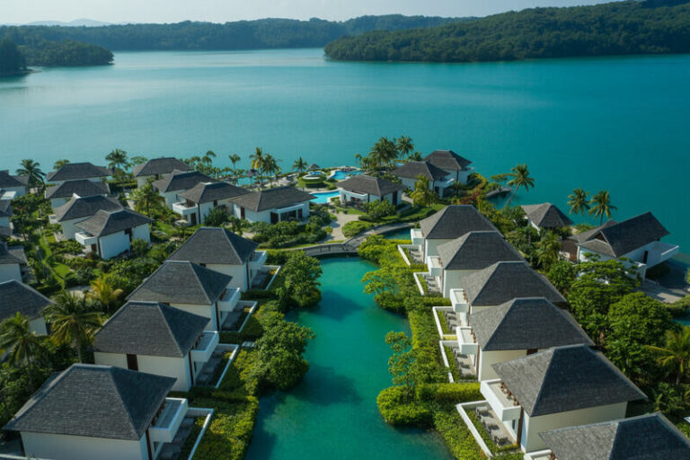 Aerial view of a tropical resort with white villas along a turquoise canal and palm trees.