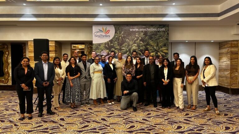 Group of professionals posing for a photo in a hotel ballroom in front of a Seychelles banner and palm imagery, 25 people in business attire.