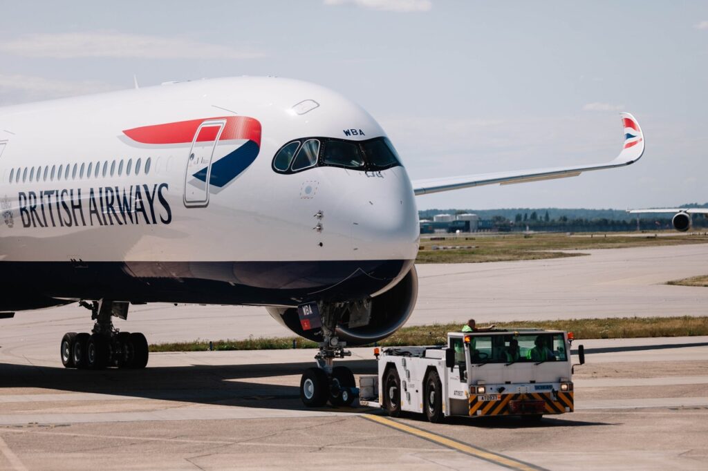 British Airways jet being pushed back by a tug on a sunny airport tarmac to prepare for taxiing.