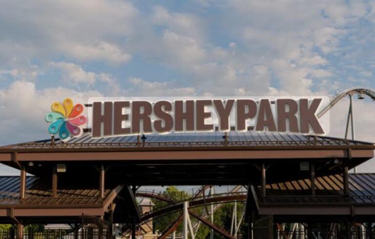 Hersheypark entrance sign with a colorful flower logo against a blue sky and cloudy backdrop.