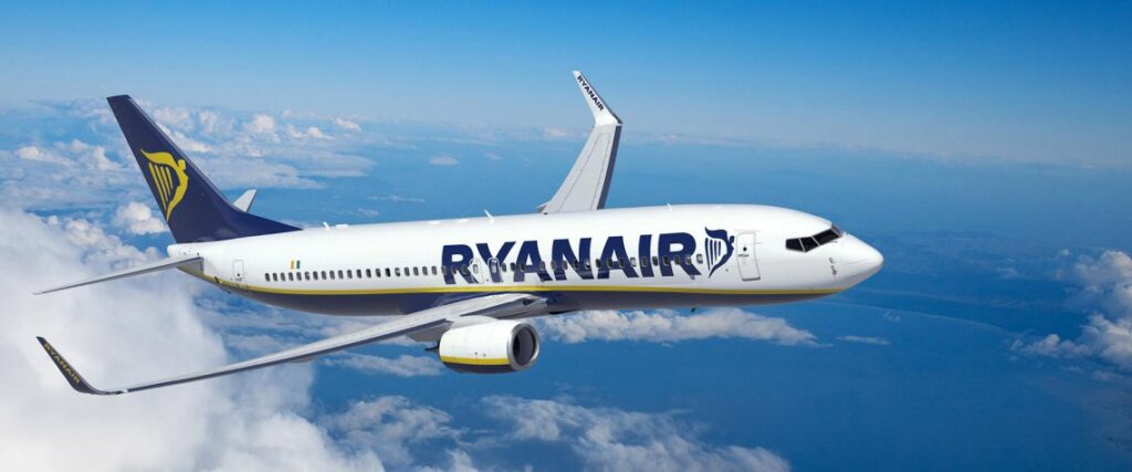 Ryanair Boeing jet in white and blue livery with yellow accents flying above clouds