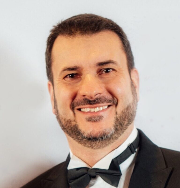 Portrait of a smiling man in a black tuxedo and bow tie, looking at the camera likely at a formal event.