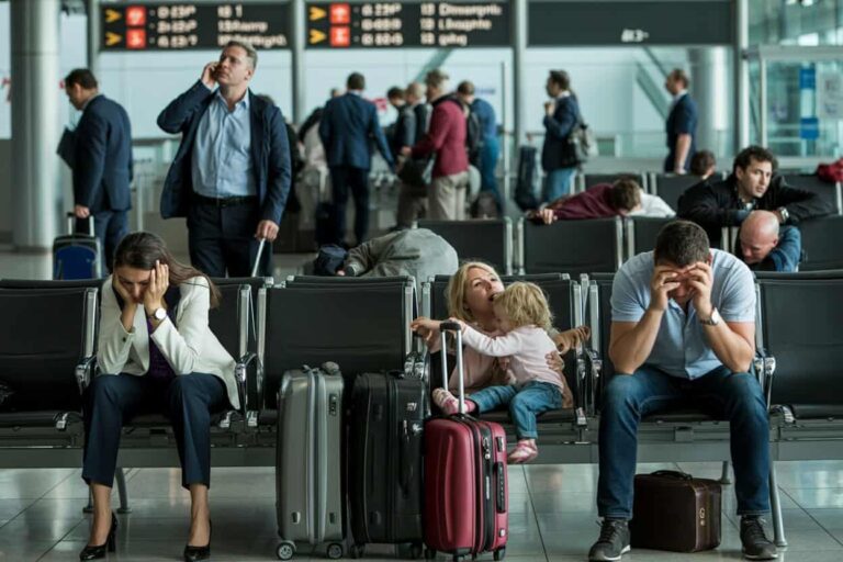 Busy airport terminal with weary travelers waiting, some on phones, others stressed and resting with luggage nearby