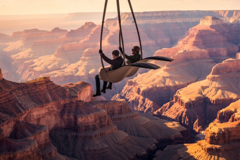Two people ride a suspended chairlift-like seat high above a canyon at sunset, holding onto the straps as they glide over the rocky landscape.