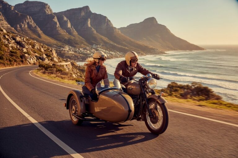 Motorcycle with a tan sidecar riding along a coastal highway with mountains in the distance at sunset. (informative)
