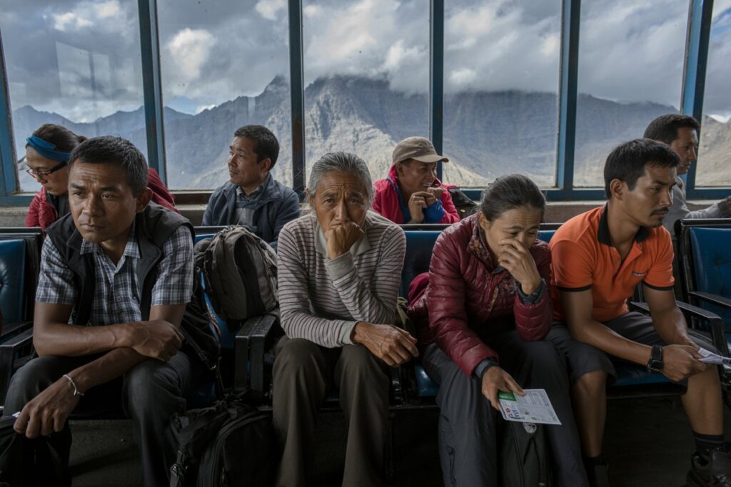 Group of travelers sitting on a bus with backpacks, gazing pensively as mountains rise outside the windows that line the cabin boundary.
