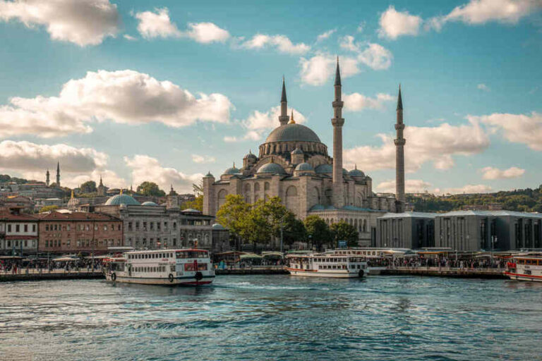 Istanbul waterfront with a grand domed mosque and two tall minarets by a busy harbor with boats.