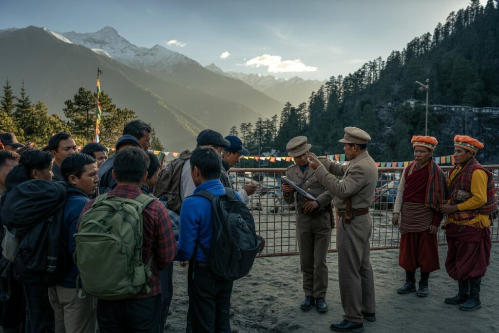 Tourists with backpacks listen to two police officers showing a map against a mountainous backdrop with prayer flags.