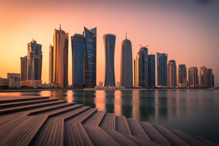Sunset over a modern city skyline with tall glass skyscrapers reflected in calm water, with wooden steps in the foreground.