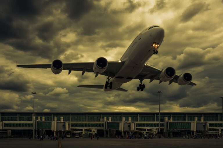 Airliner lifting off from runway in front of a terminal under dramatic cloudy skies, with passengers visible near the gate area below.