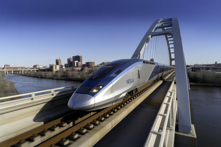 High-speed passenger train on a modern arch bridge crossing a river with a city skyline in the distance.