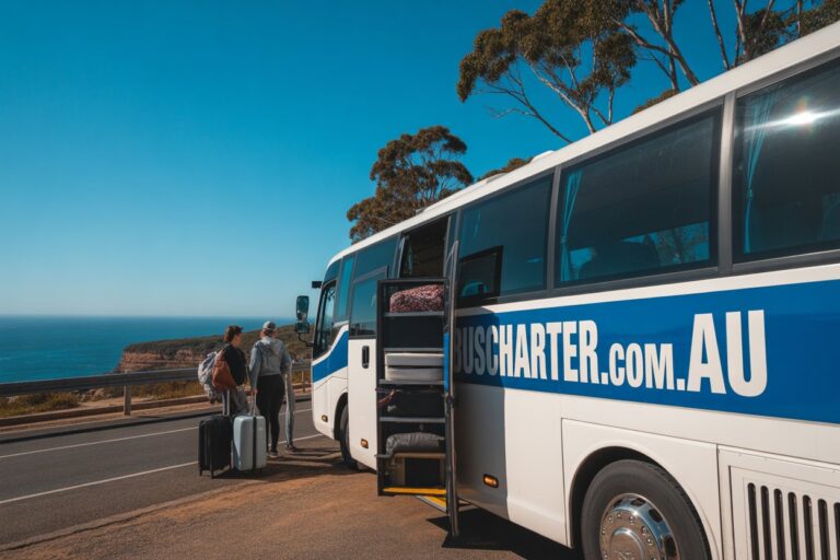 Two travelers with rolling suitcases stand beside a white and blue bus on a coastal road overlooking the ocean.