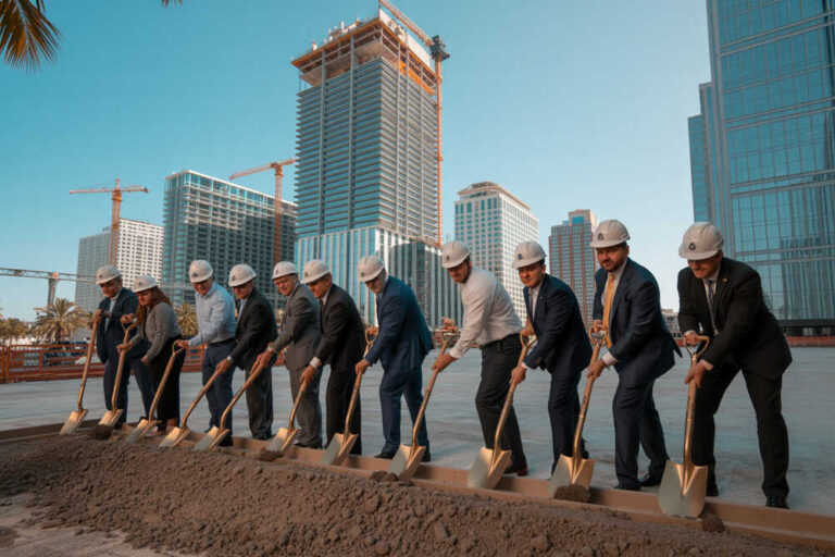 Groundbreaking ceremony with businesspeople in suits and hard hats shoveling dirt at a construction site in a cityscape with tall buildings.