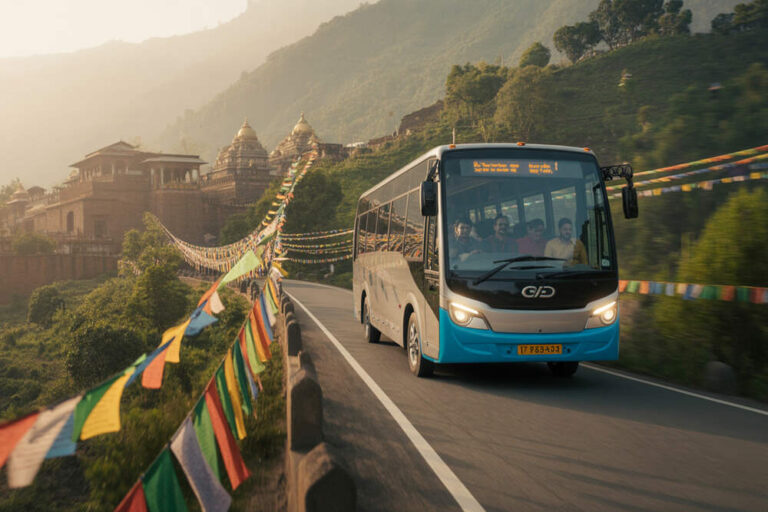 Tour bus driving along a winding mountain road lined with colorful prayer flags, with temple ruins on the hillside in the distance.