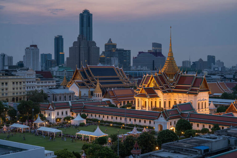 Bangkok Grand Palace illuminated at dusk with modern city skyline in the background, left and center.