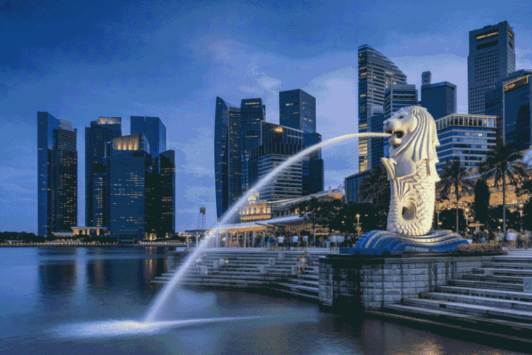 Merlion statue spouting water into Marina Bay with Singapore's skyline at dusk behind it