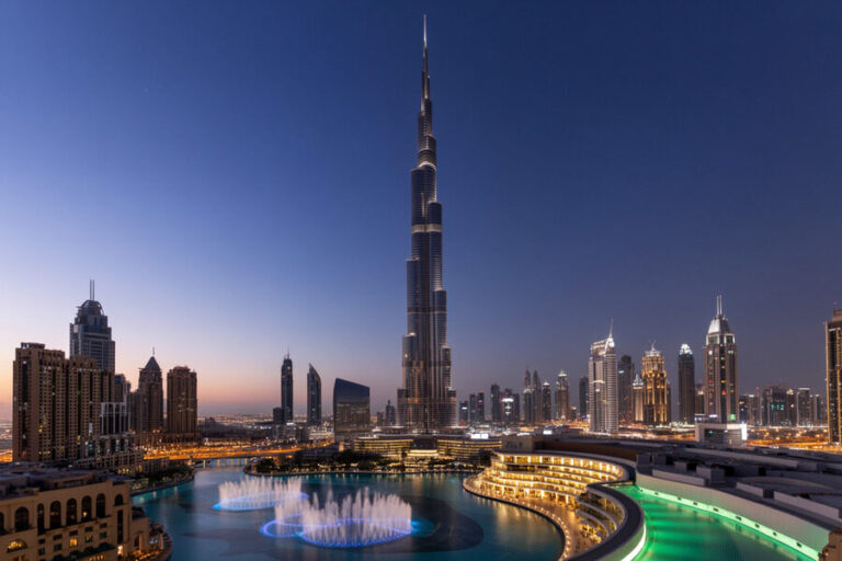 Dubai skyline at dusk featuring Burj Khalifa and illuminated fountain pool along a curved promenade