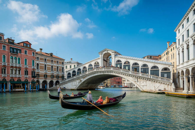 Gondolas glide on the Grand Canal beneath the Rialto Bridge in Venice, with colorful historic buildings along the water.