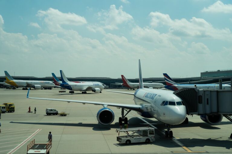 Large white commercial airliner at a gate with a jet bridge attached, other planes parked on the tarmac under a blue sky with clouds. (Informative scene of an active airport.)