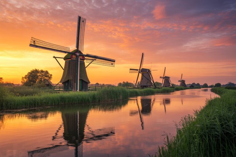 Row of traditional windmills along a calm waterway at sunset, reflected in the canal, with grassy banks.
