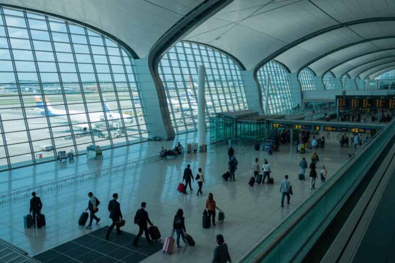 Interior of a modern airport terminal with travelers and rolling luggage, curved glass walls and high arches for windows.