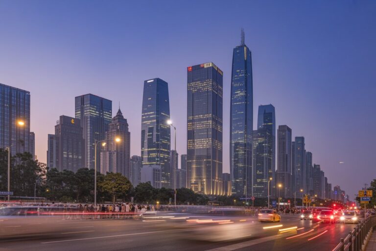 Evening city skyline with tall glass skyscrapers and light trails from moving cars in the foreground.