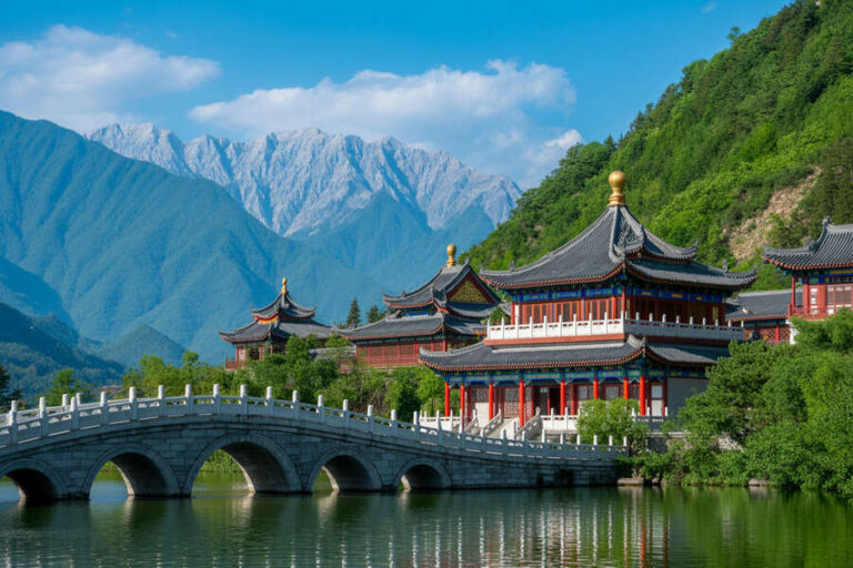 Traditional Chinese temple buildings along a lakeshore with a curved stone bridge, green hills, and distant mountains.