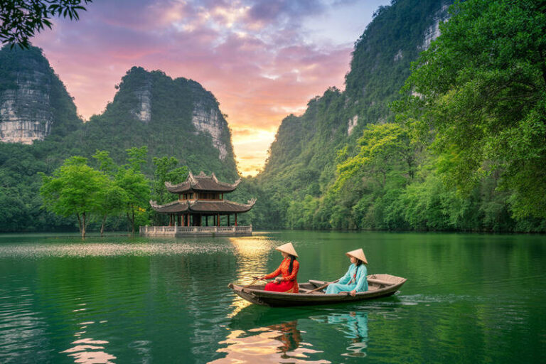 Two travelers in a small wooden boat on a calm emerald lake, with a traditional pavilion and dramatic limestone cliffs at sunset.