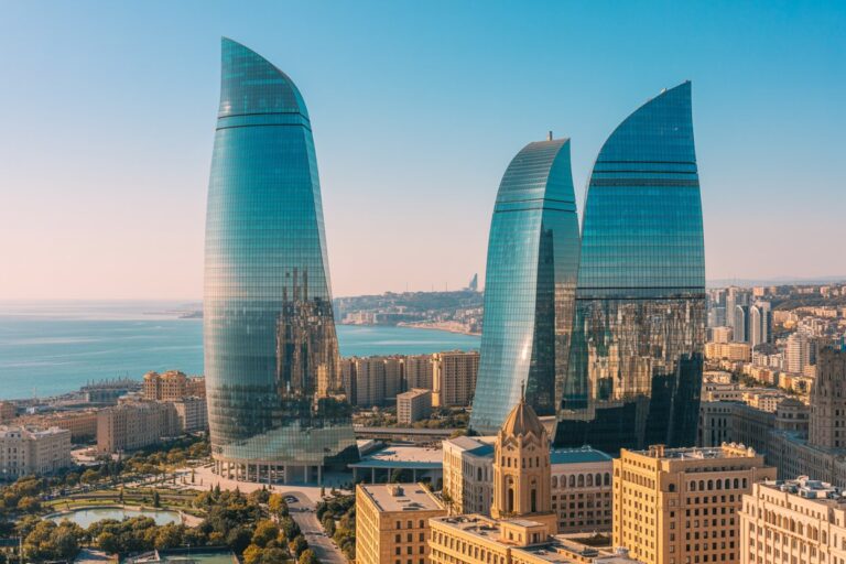 Three curved glass skyscrapers (Flame Towers) overlook a coastal city by the Caspian Sea, with historic buildings in the foreground and a clear blue sky.