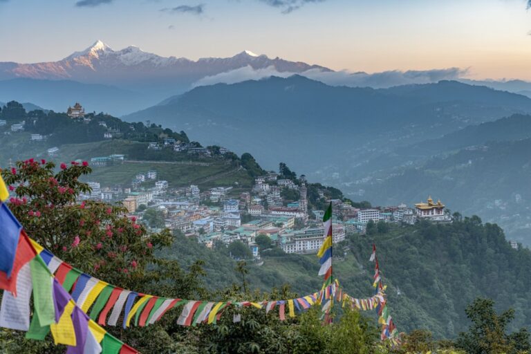 Hillside town in the Himalayas with colorful prayer flags in the foreground and misty mountains in the distance at sunset.