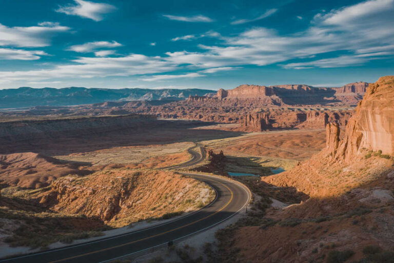 Winding two-lane road through a red rock desert canyon under a blue sky.