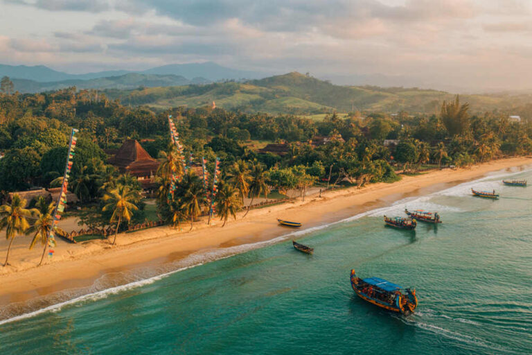 Tropical beach with palm trees, colorful flags, and small boats along turquoise sea at sunset piece of coastline.
