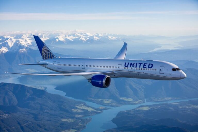 United Airlines jet flying over snow-capped mountains and a winding blue river below, during clear weather