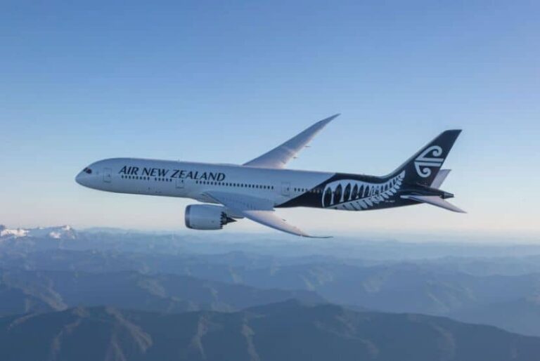 Air New Zealand passenger airplane in flight over a mountain landscape, tail displays the fern logo.