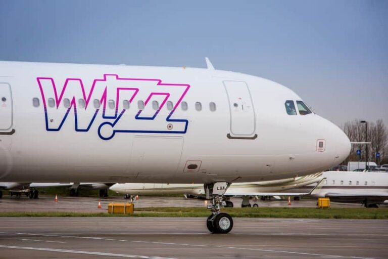 Close-up of a white passenger airplane on the tarmac with a pink-and-blue Wizz Air logo on the fuselage near the nose.
