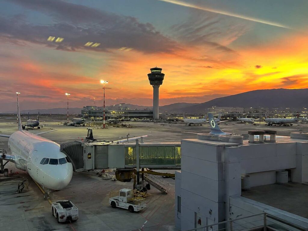 Airplane at the gate during sunset with the control tower and distant hills in view