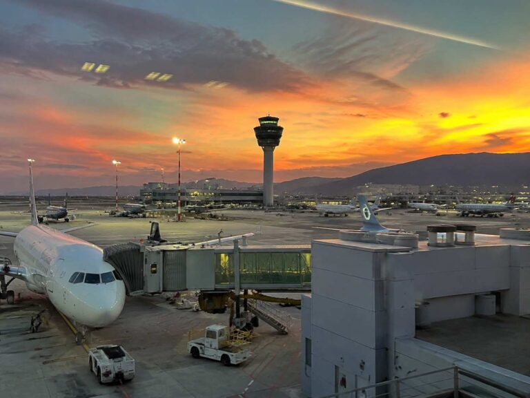 Airplane at the gate during sunset with the control tower and distant hills in view