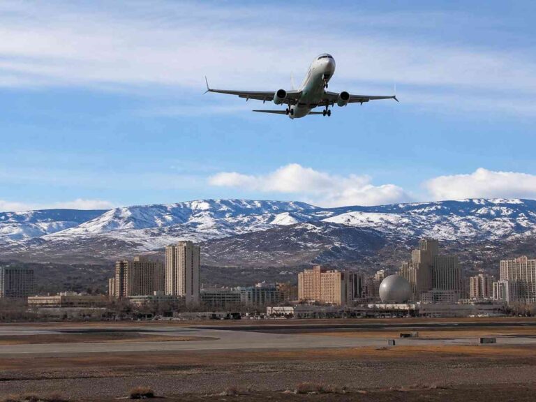 Airplane approaching for landing above a city with snow-capped mountains in the background and clear blue sky, runway in foreground