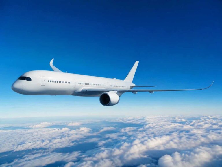 White commercial airplane flying above clouds in a clear blue sky.