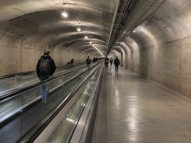 Underground pedestrian tunnel with a moving walkway, people walking along the sides.