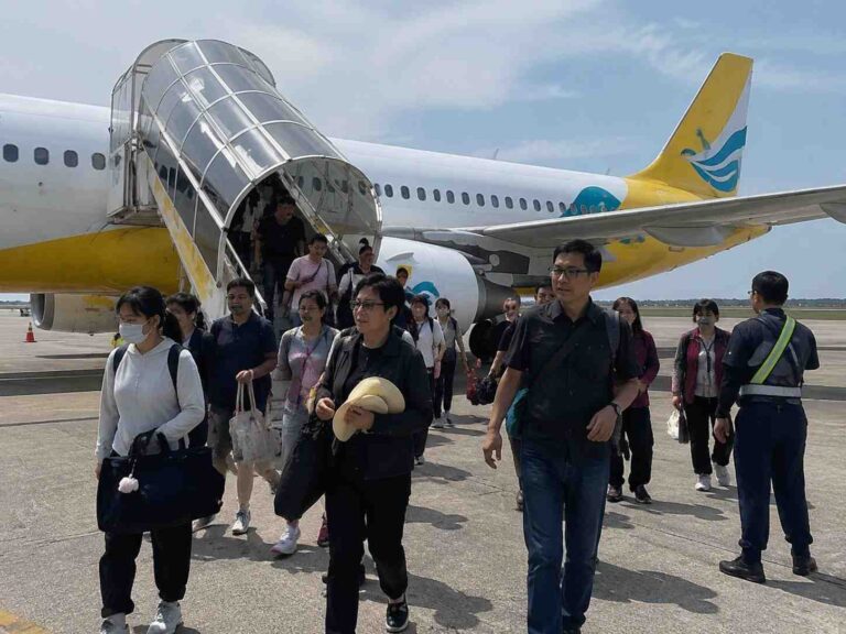 Group of travelers walking down a glass-enclosed mobile staircase from a white and yellow airplane on a sunny tarmac.